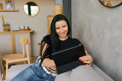 Beautiful caucasian brunette dressed in a black t-shirt is sitting on the sofa in the living room