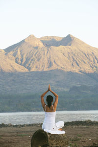 Woman practicing yoga on field against mountain