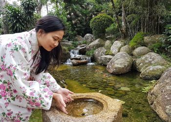 Smiling woman wearing kimono while putting hand in water at park