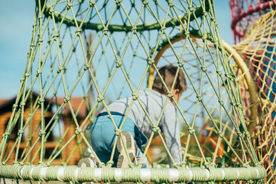 Low angle view of man sitting on metal fence