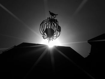 Low angle view of silhouette building and weather wane against sky on sunny day