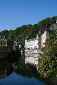 Buildings by river against clear blue sky