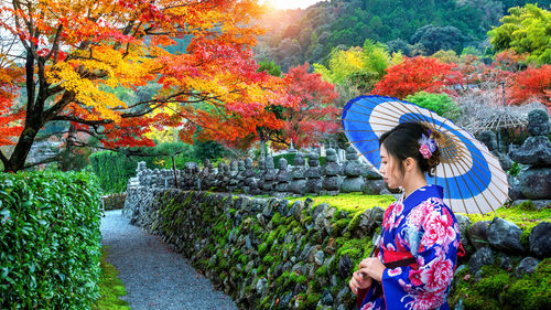 Woman standing on footpath amidst trees during autumn