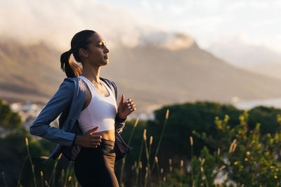 Side view of young woman standing against mountain