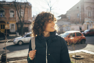 Smiling woman looking away while standing on street in city