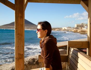 Side view of thoughtful woman sitting on bench looking at sea against sky