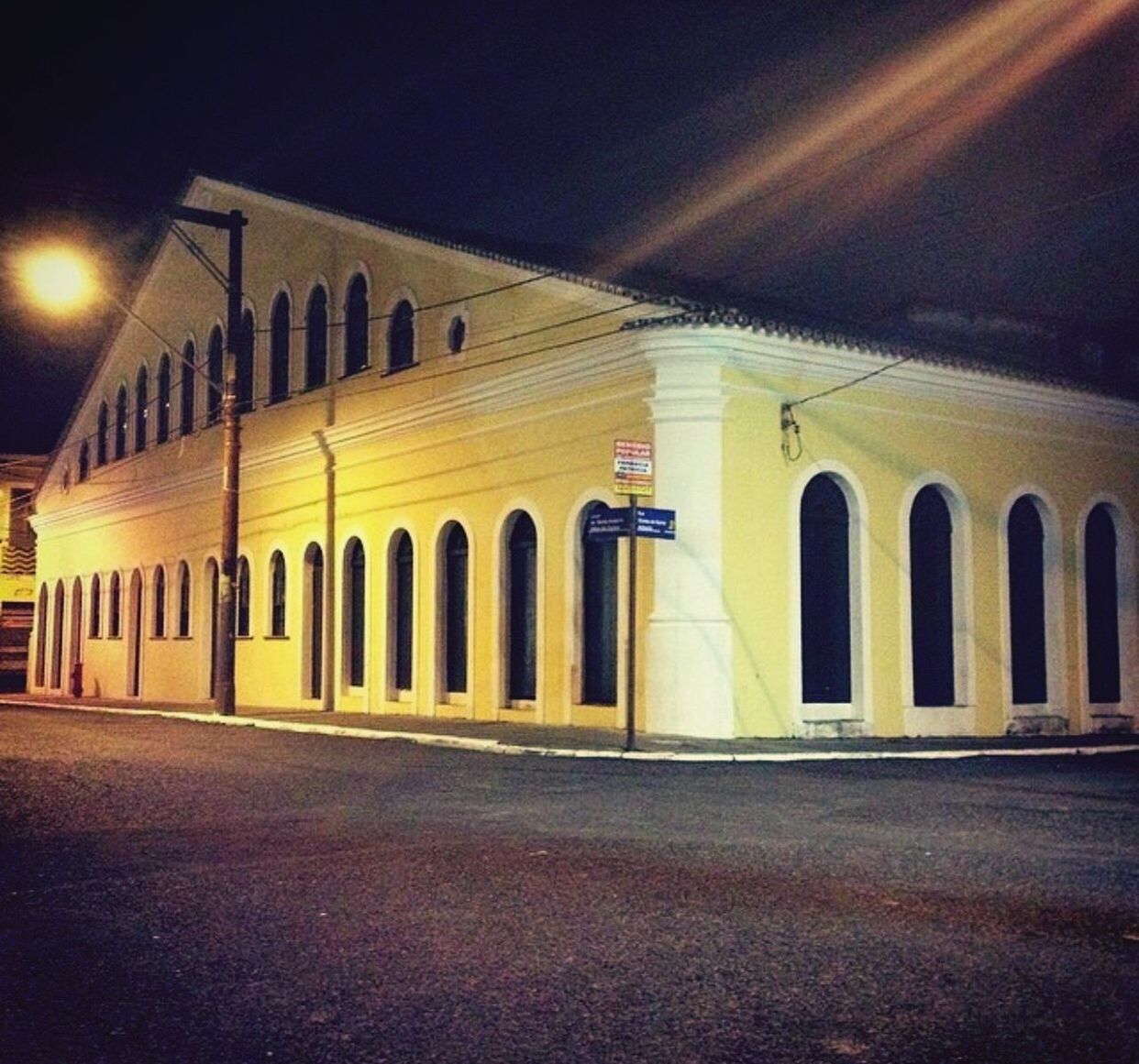 ILLUMINATED ROAD BY BUILDING AT NIGHT