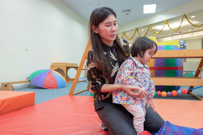 Cute girl with teacher on carpet in kindergarten