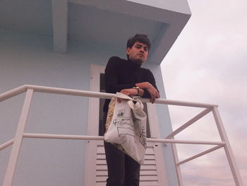 Low angle portrait of young man standing by railing in balcony