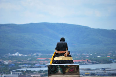 Rear view of statue against building and mountains