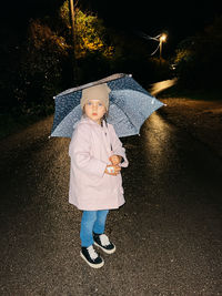 Full length of young woman with umbrella on road