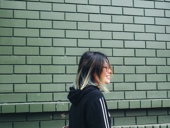 Side view of young woman standing against brick wall