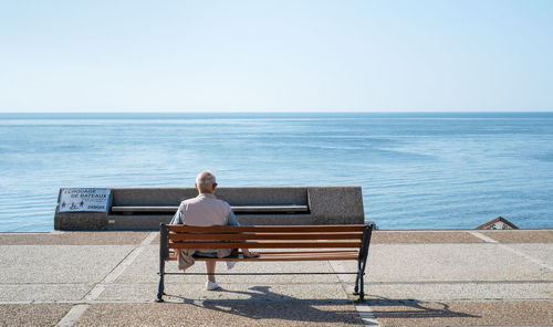 Rear view of man sitting on bench against sea