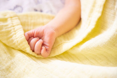 Newborn caucasian premature baby hand on pastel yellow soft muslin blanket soft focus. copy space