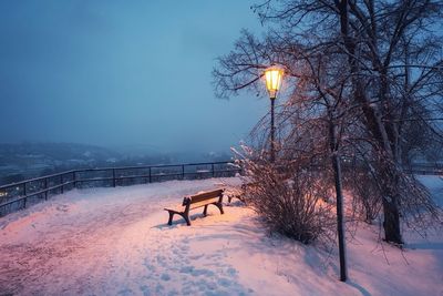 Snow covered park bench against sky during winter