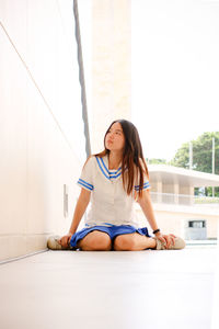 Young woman sitting against wall