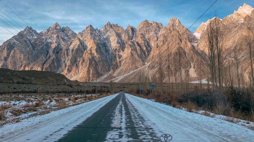 Snow covered road by mountains against sky