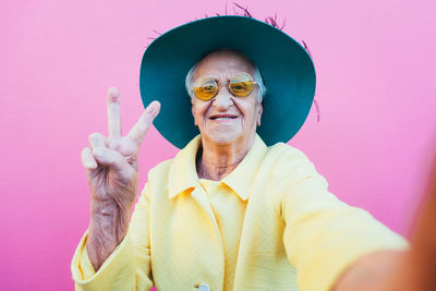 Senior woman wearing hat gesturing against pink background