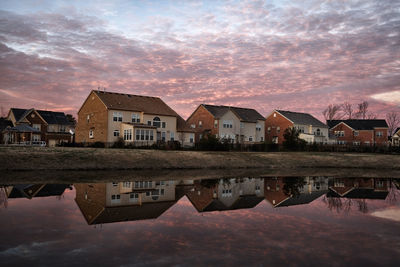 Buildings by lake against sky during sunset