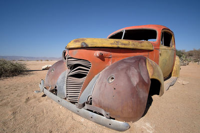 Abandoned car on desert against sky