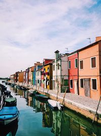 Boats moored in canal by buildings against sky