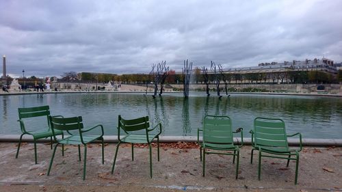 Chairs by river against sky in city