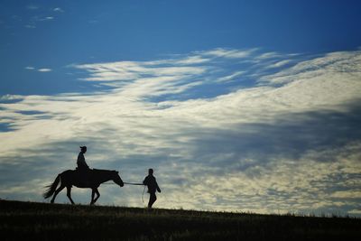 Man holding harness by woman riding horse on field