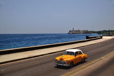 Car on road by sea against clear sky