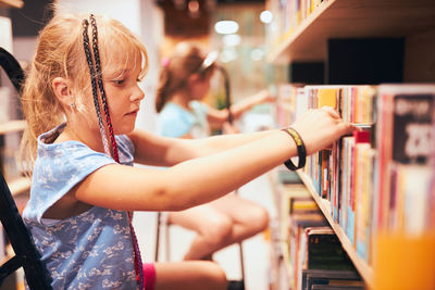 Schoolgirls looking for books in school library. students choosing set books. elementary education