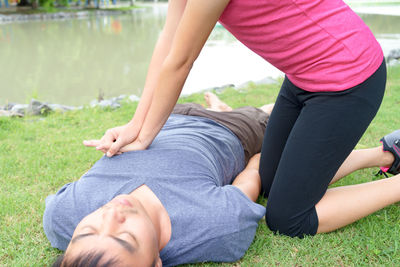 Low section of woman giving cpr to man lying in grassy field