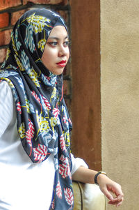 Young woman looking away while standing against wall