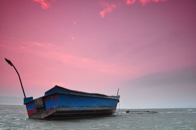 Boat moored on sea against sky during sunset