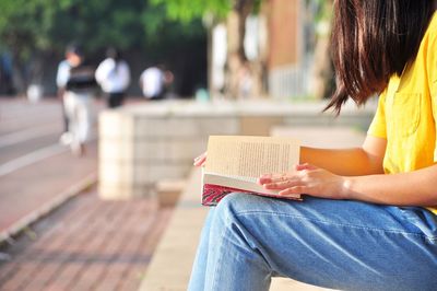 Midsection of woman reading book while sitting on bench