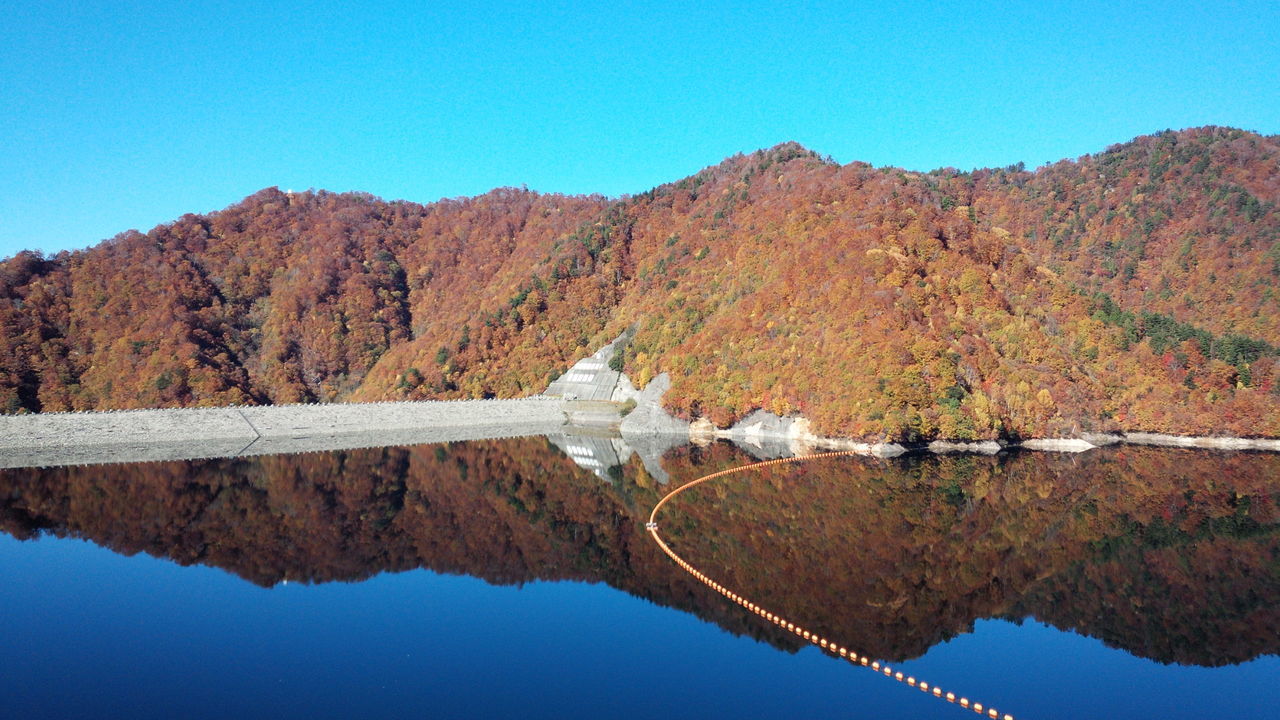 mountain, clear sky, water, blue, lake, reflection, tranquility, tranquil scene, scenics, beauty in nature, mountain range, nature, tree, landscape, copy space, transportation, day, waterfront, non-urban scene, river