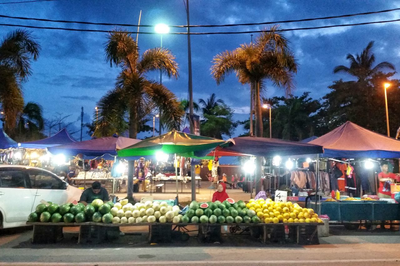 illuminated, market, retail, market stall, for sale, tree, sky, incidental people, men, choice, lighting equipment, abundance, display, street, night, variation, outdoors, building exterior, food and drink