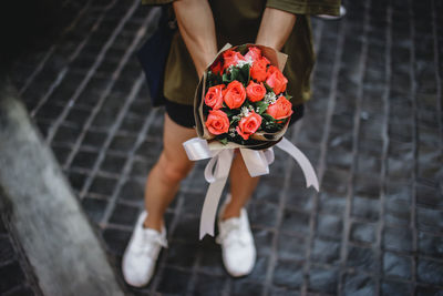 Low section of woman holding rose bouquet standing on footpath