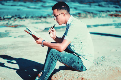Side view of man reading book at beach