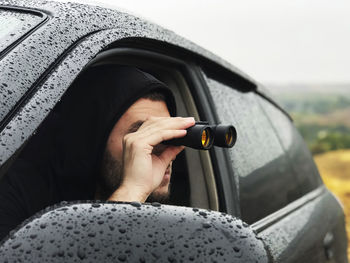 Close-up of man looking through binoculars while siting in car during rainy season