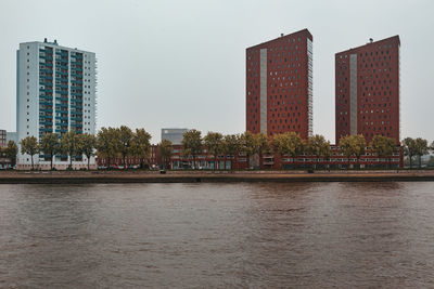 Modern buildings by river against sky in city