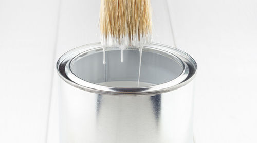 Paint brush with white paint flowing into a can on a white wooden background close-up