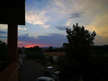 Silhouette trees by road against sky during sunset