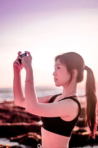 Young woman standing on beach against sky during sunset