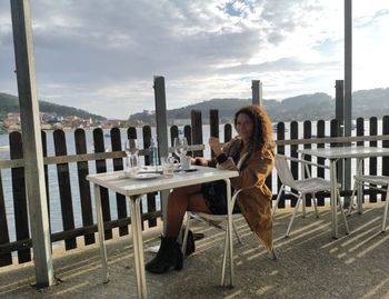 Woman sitting on chair at table against sky