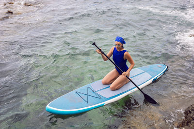 Athlete woman in blue swimsuit and bandana on stand up paddle board. sup surfing