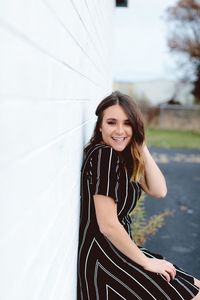 Side view portrait of young woman standing by white wall