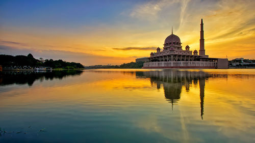 Mosque reflecting on calm lake against sky at sunset