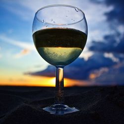 Close-up of white wine on sand at beach during sunset