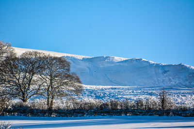 Scenic view of snow covered mountains against clear blue sky