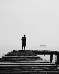 Rear view of man standing on pier over sea against sky