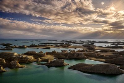 Rocks on beach against sky during sunset